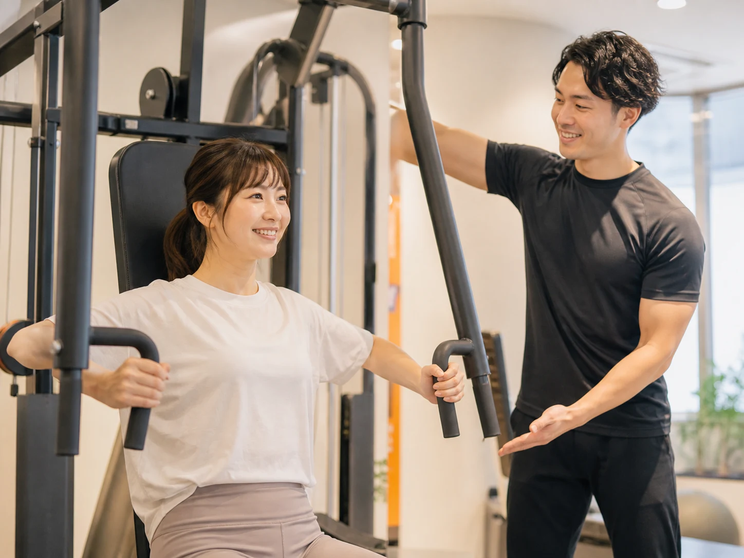 トレーナーに見守られながらマシン運動を始める女性